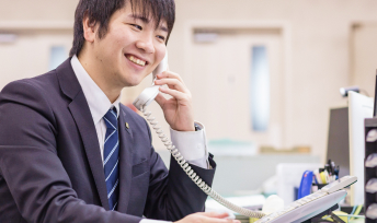 写真：デスクの電話で笑顔で話している営業の三宅 優河