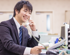 写真：デスクの電話で笑顔で話している営業の三宅 優河